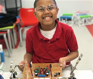 PLA STEM student smiling in front of engineering board 